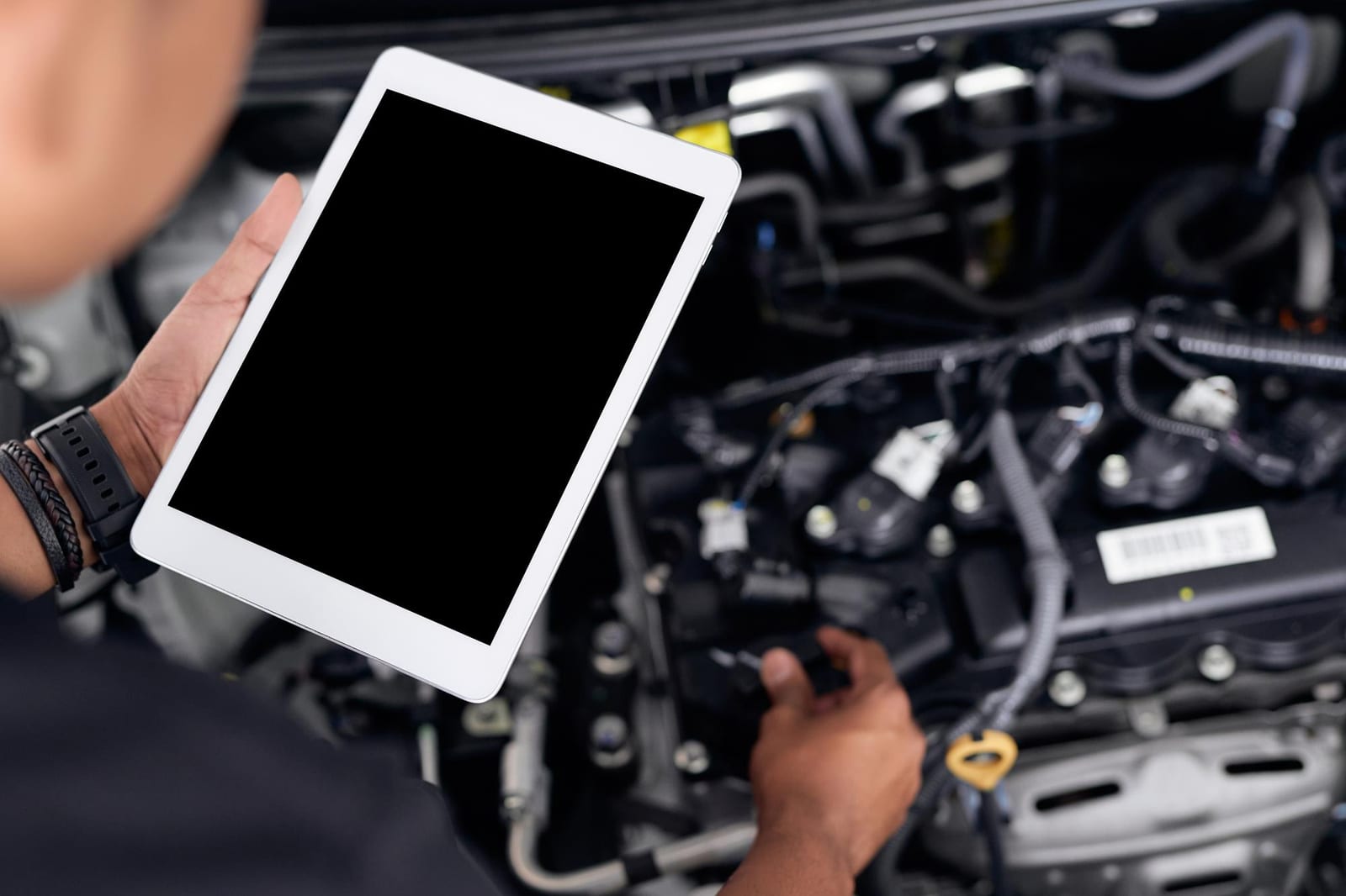 Um técnico segura um tablet com a tela em branco sobre o compartimento do motor de um carro aberto.